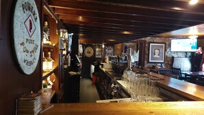 A bar area with a long counter, shelves with bottles, and a mounted television. - The Oyster House (Clarinbridge)