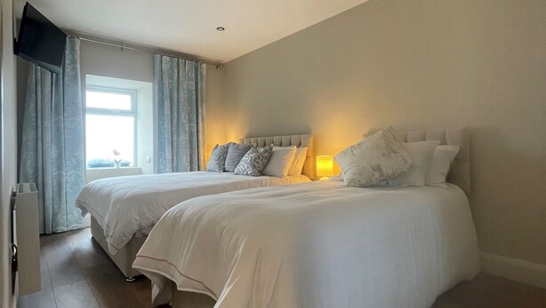 A bedroom with two beds, a flat-screen TV mounted on the wall, and a window with curtains. - The Oyster House (Clarinbridge)