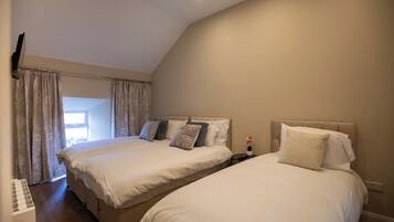 A bedroom with two beds, a window, and a nightstand with a lamp.