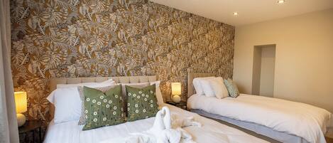 A hotel room with two beds, a floral wallpaper, and a robe on the bed.