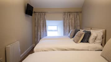 A bedroom with two beds, a TV mounted on the wall, and a window with curtains.