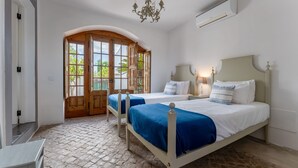 Un dormitorio con dos camas, un amplio ventanal arqueado, un candelabro y un ventilador de techo.