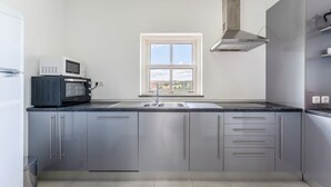 Una cocina moderna con armarios grises, un lavamanos de acero inoxidable, un microondas integrado y una ventana con vistas al campo.