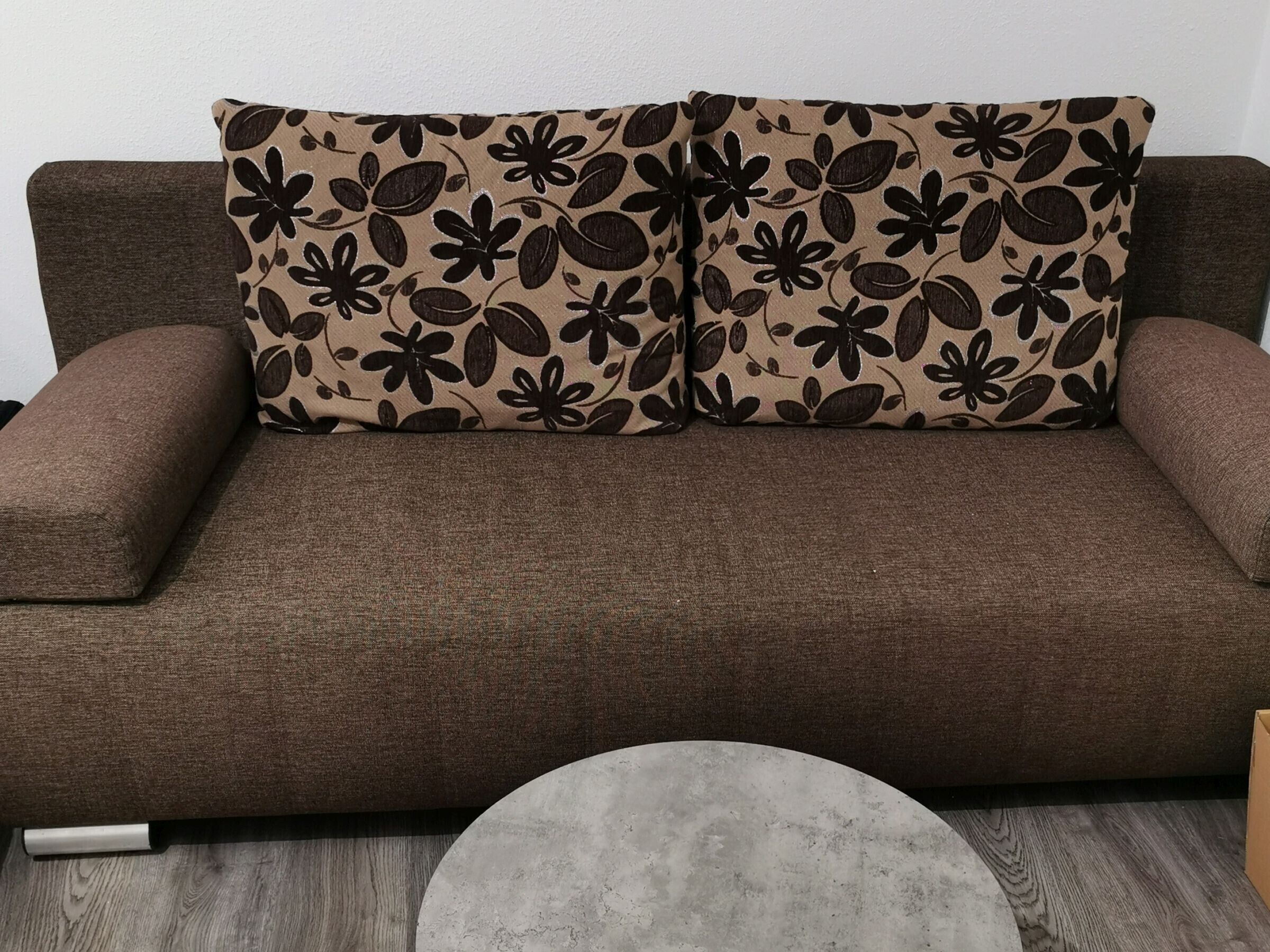 En brun sofa med puder med blomstermønster og et rundt, gråt sofabord.