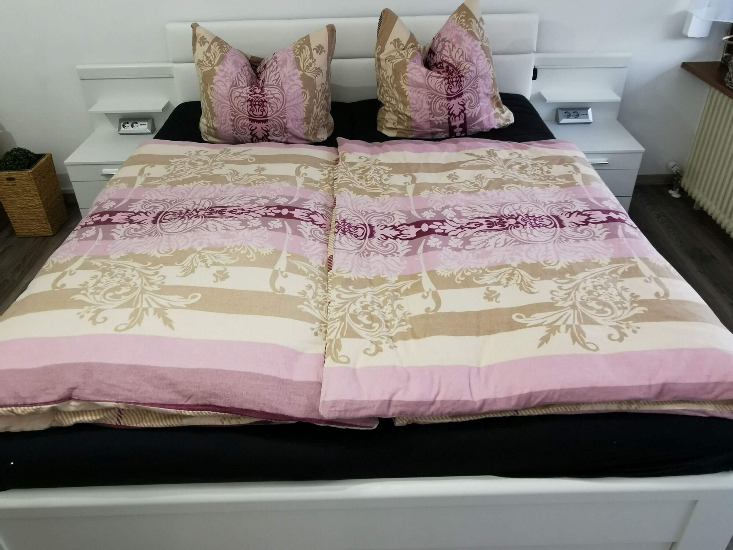 Un lit avec une couvre-lit à motifs, deux oreillers, une table de chevet avec une lampe et un radiateur.