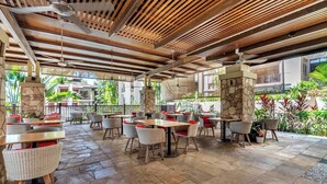 Un patio al aire libre con suelo de piedra, sillas de mimbre y mesas con cojines rojos.