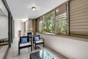 Un balcone con due poltrone in vimini, un tavolino in vetro e una pianta in vaso.