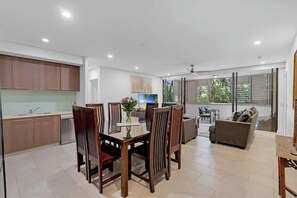 Une cuisine moderne avec des meubles en bois, un coin repas avec une table et des chaises, et un salon avec un canapé et un téléviseur.