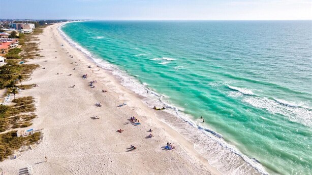 Une plage aux eaux turquoise et limpides, un rivage sablonneux et des bâtiments qui bordent la côte.