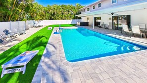 Una piscina con zona de patio, césped y una casa al fondo.