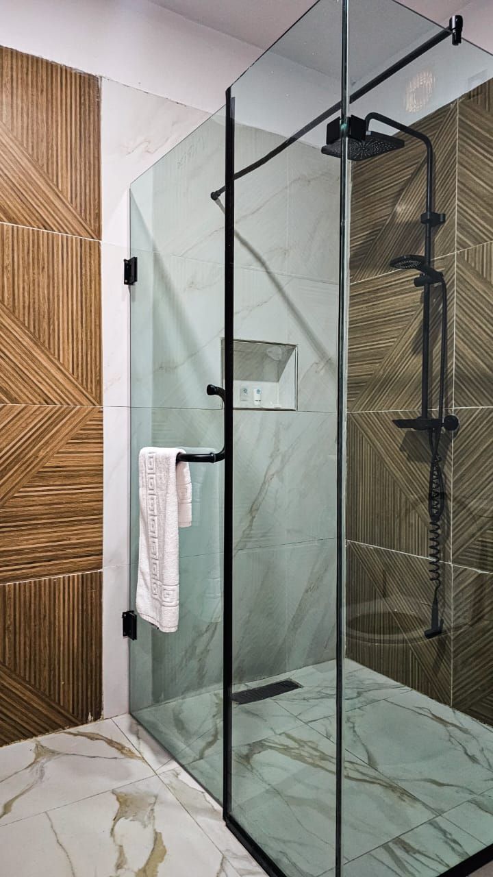 A glass-enclosed shower with a handheld showerhead, a towel rack, and a control panel.
