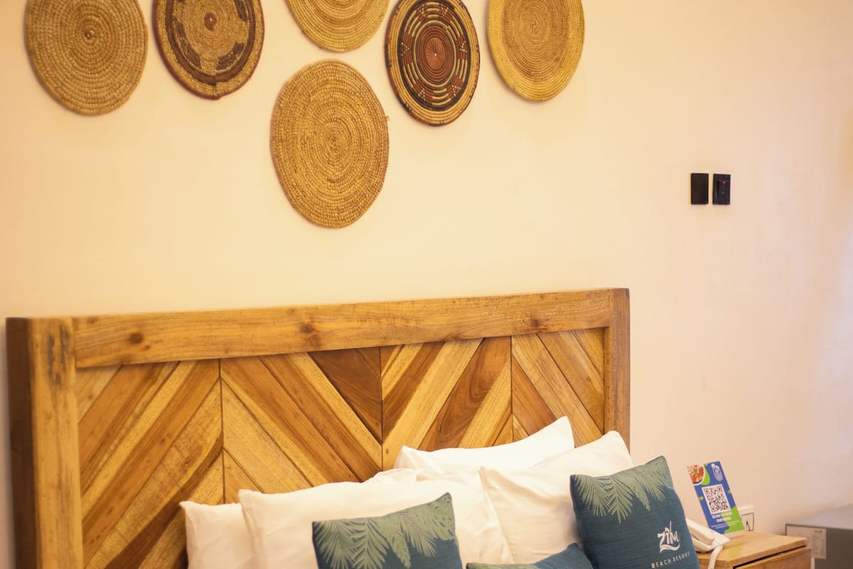 A bed with a wooden headboard, white bedding, and decorative pillows with palm leaf patterns.