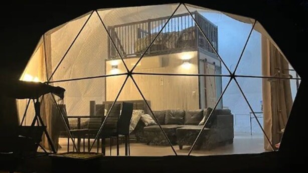 Een geodetische koepelstructuur met een zithoek binnenin, een balkon en uitzicht op het omliggende landschap.
