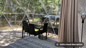 Een geodetische koepelstructuur met een tafel en stoelen, met uitzicht op een bebost gebied.