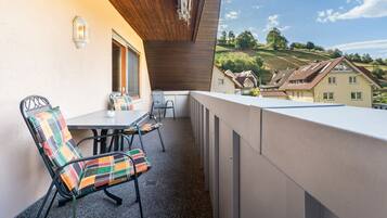 A balcony with a table and chairs, a view of a hillside with houses, and a wooden ceiling.