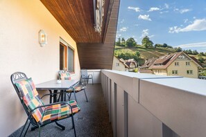Ein Balkon mit Tisch und Stühlen, Blick auf eine Hügelslandschaft mit Häusern und eine Holzdecke.