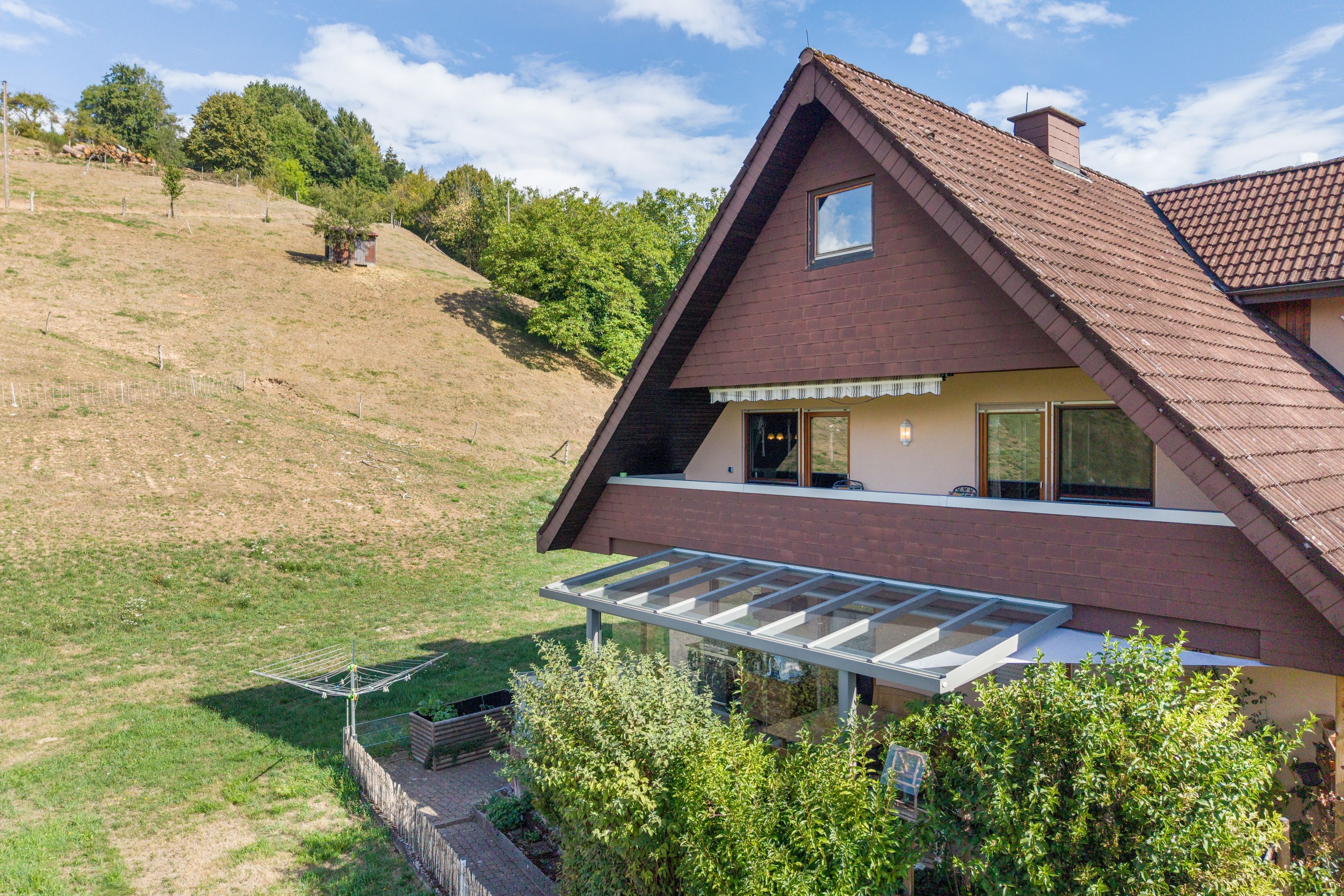 Ein zweistöckiges Haus mit geneigtem Dach, einem sichtbaren Dachboden und einem großen Glasbalkon.
