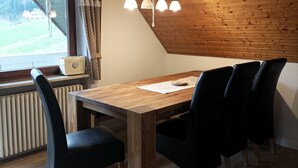 Uma área de refeições com mesa de madeira e cadeiras pretas, um radiador e uma janela com cortinas.