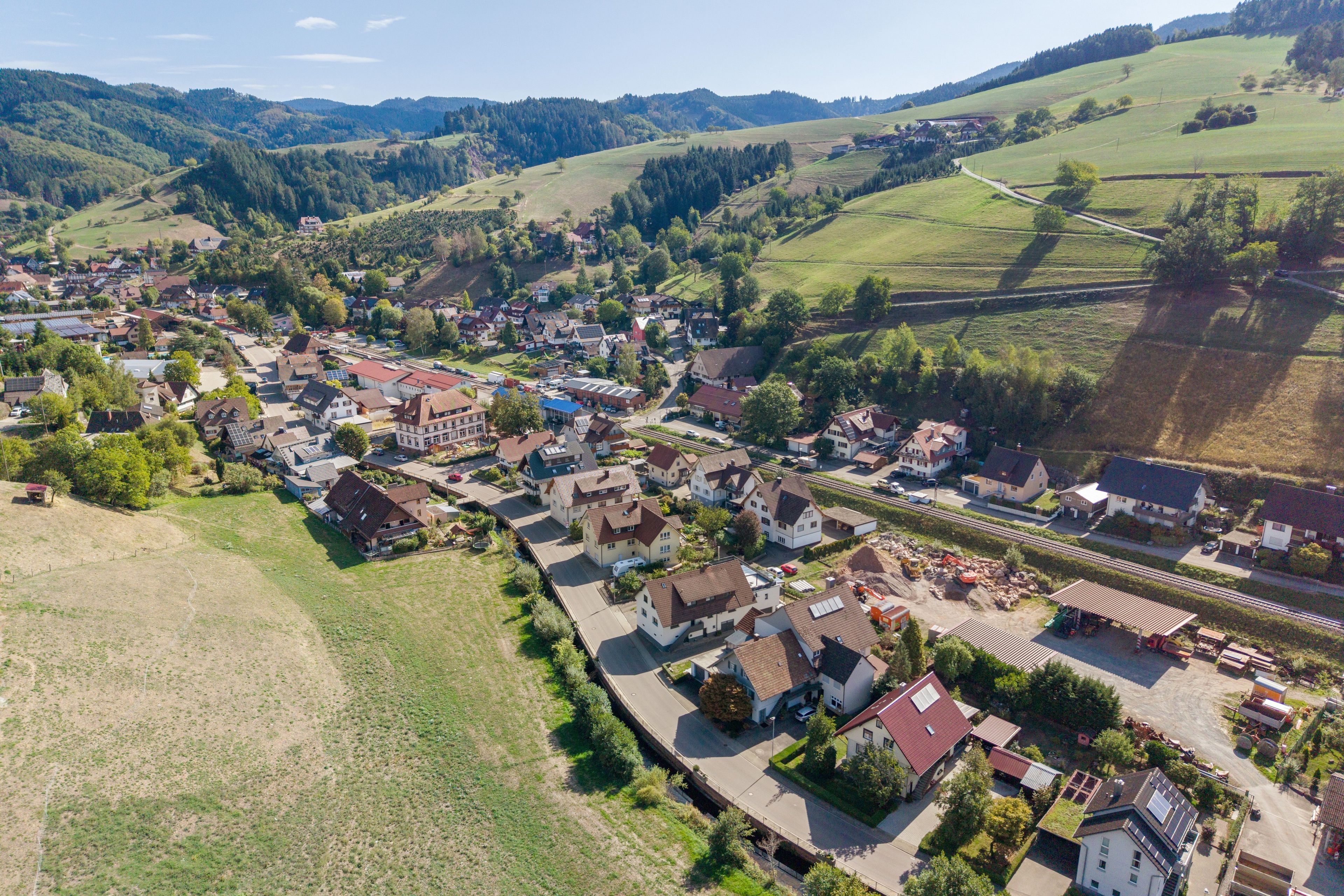 A small town with a mix of residential and commercial buildings, a railway line, and rolling hills in the background.