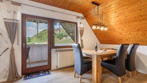 Een eethoek met een houten tafel en stoelen, uitzicht op een heuvel door een raam en een radiator onder het raam.