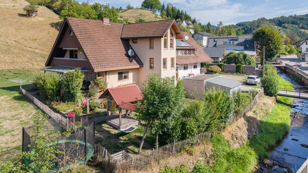 Een twee verdiepingen tellend huis met een schuin dak, een schotelantenne en een kleine tuin.