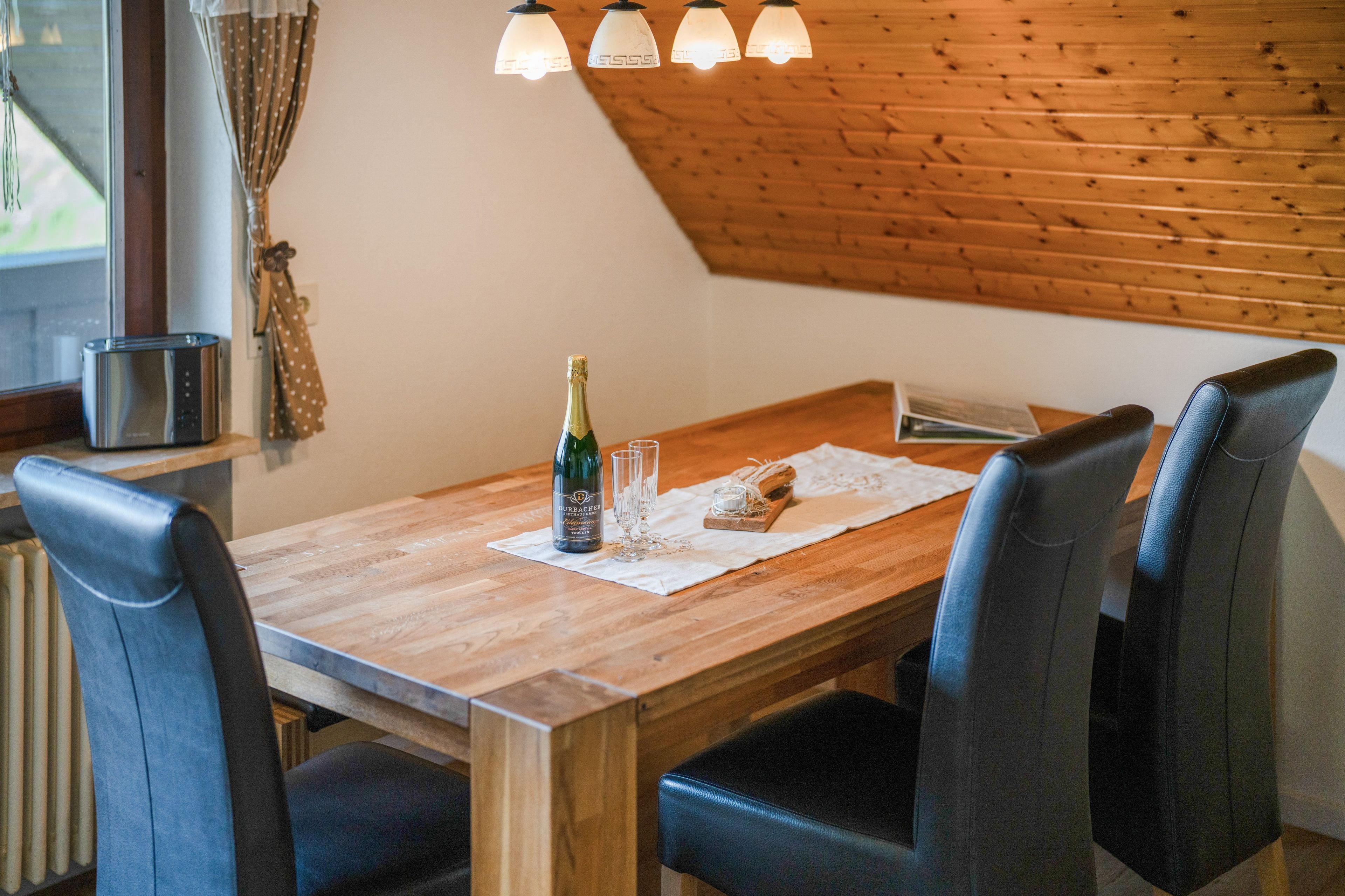 Ein Holztisch mit vier Stühlen, einer Champagnerflasche und Gläsern auf einer Tischdecke.