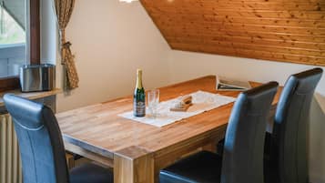 A wooden dining table with four chairs, a bottle of champagne, and glasses on a placemat.