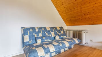 A corner room with a sloped ceiling, a radiator, and a sofa with a geometric patterned cover.