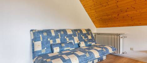 A corner room with a sloped ceiling, a radiator, and a sofa with a geometric patterned cover.