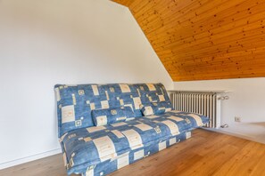 A corner room with a sloped ceiling, a radiator, and a sofa with a geometric patterned cover.