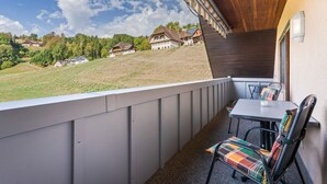 Een balkon met uitzicht op huizen op een heuvel, een tafel met stoelen en een houten plafond.