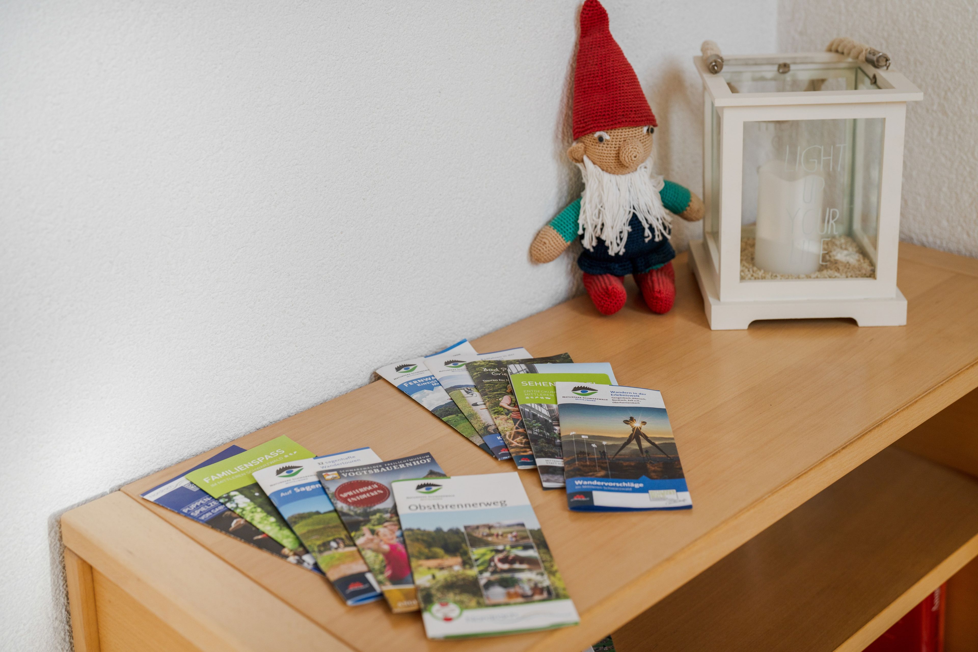 A wooden table with a gnome figurine, a lantern, and a collection of travel brochures.
