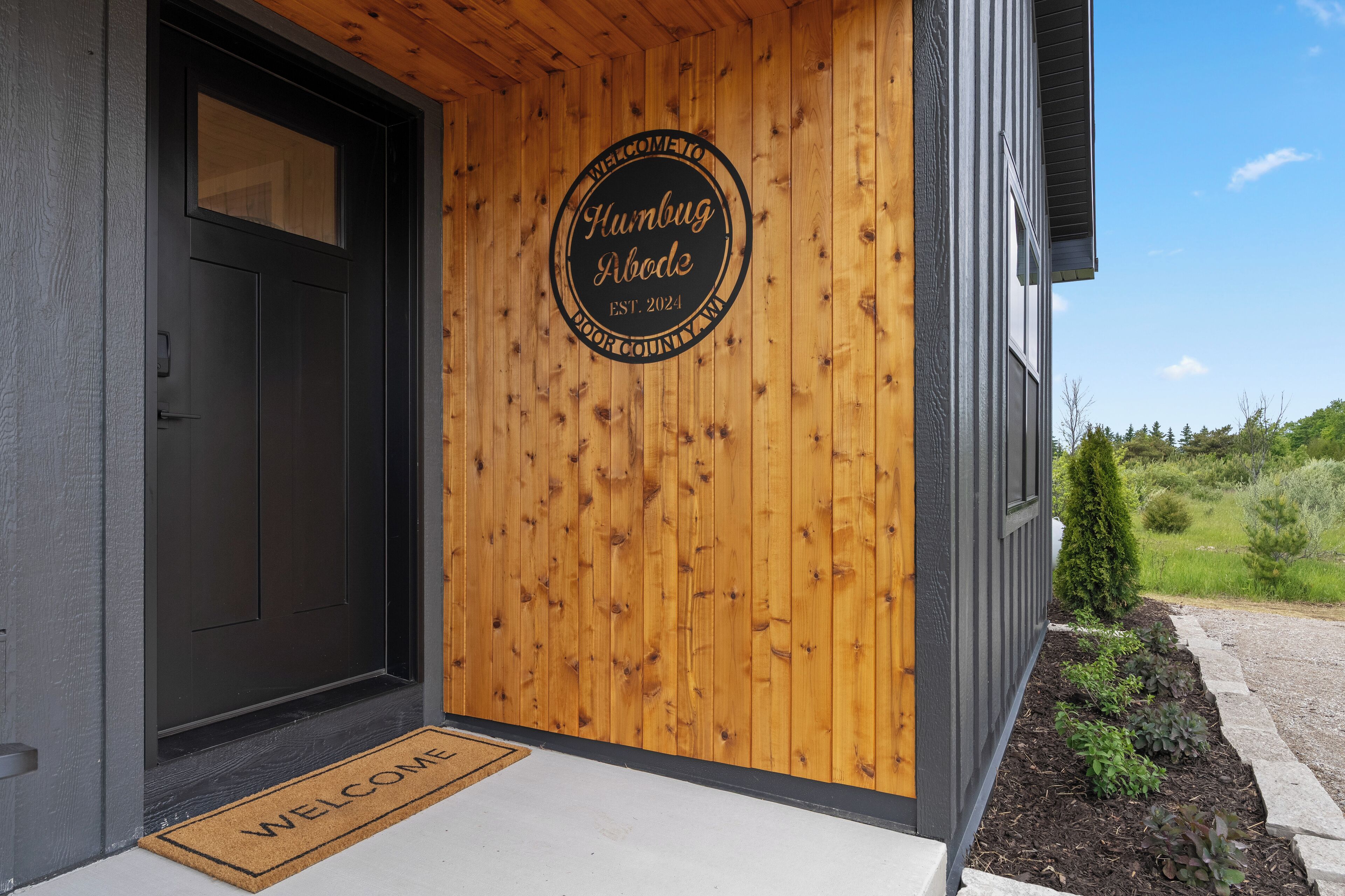Puerta de madera con un cartel de bienvenida y felpudo.