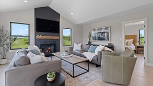 Ein modernes Wohnzimmer mit Kamin, Sofas, einem Couchtisch und großen Fenstern mit Blick ins Freie.