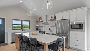 Cocina moderna con armarios blancos, electrodomésticos de acero inoxidable, una isla grande con taburetes de bar e iluminación colgante.