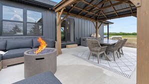Eine Terrasse im Freien mit Feuerstelle, Sitzgelegenheit und überdachtem Essbereich.