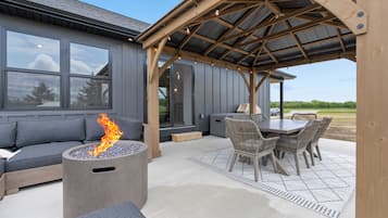 Un patio exterior con una fogata, zona de estar y un espacio de comedor cubierto.