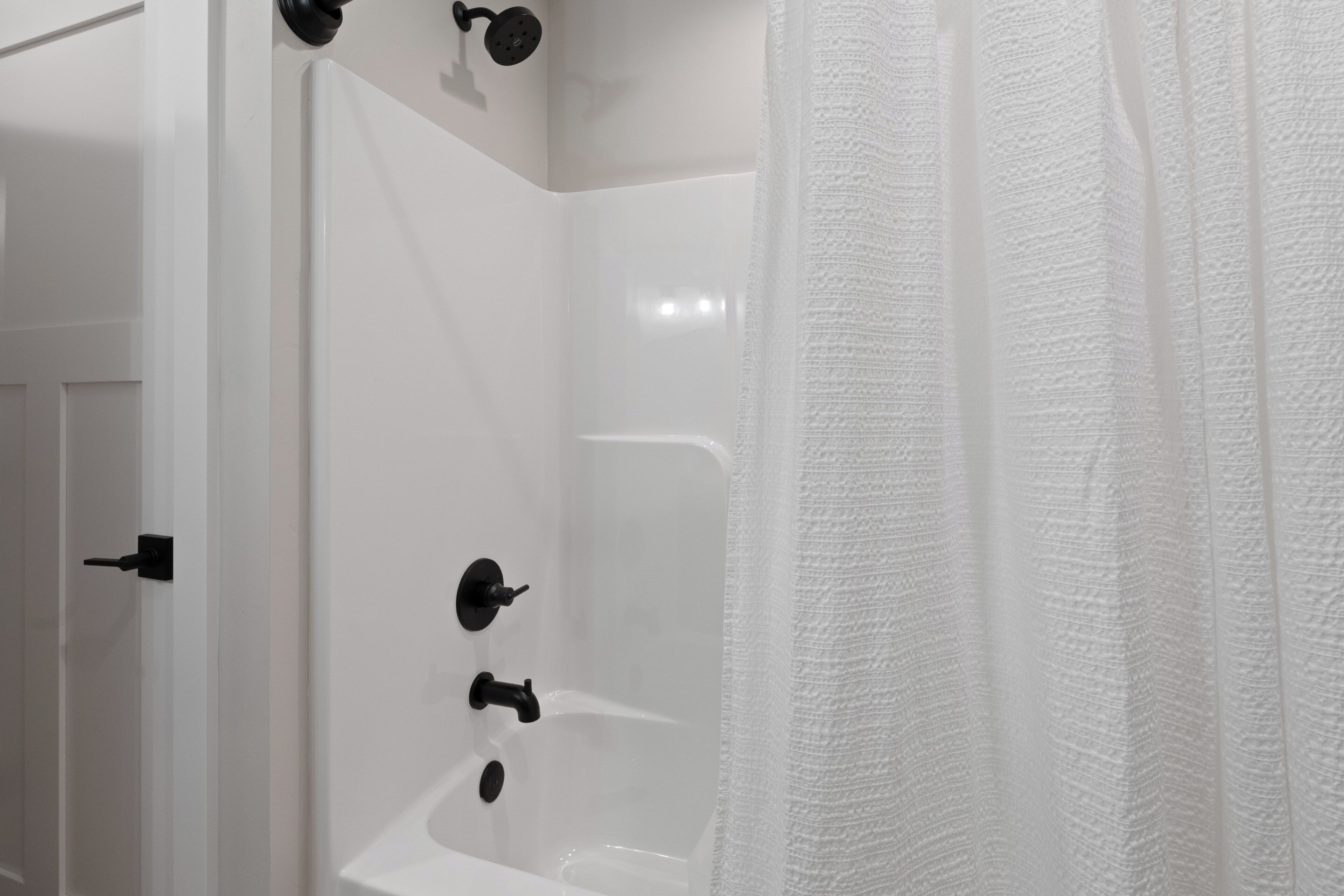 Baño blanco con bañera, ducha y toallero.