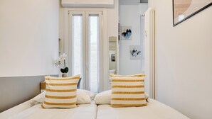 Une chambre à coucher avec un lit, deux coussins à rayures, une table de chevet, un vase avec des fleurs et une porte donnant sur une autre pièce.