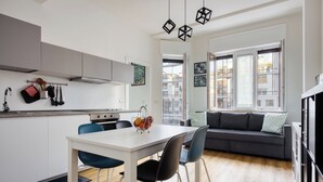 Une cuisine moderne avec des meubles blancs, une table à manger avec des chaises et un canapé gris dans l’espace salon.
