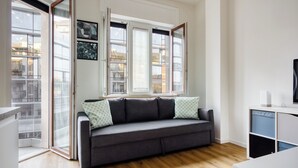 Un salon moderne avec un canapé gris, un téléviseur et une fenêtre équipée de stores.
