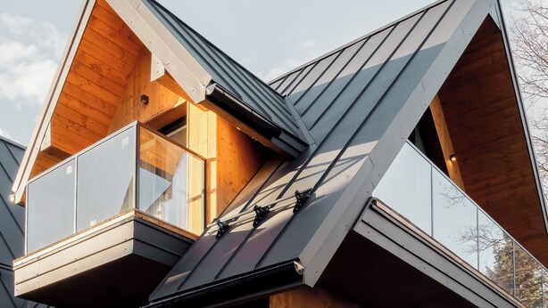 Een modern huis met een schuin dak, houten gevel en grote glasramen.