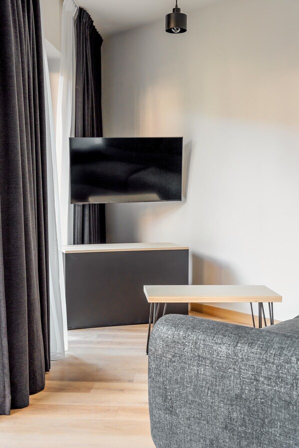 A modern living room with a flat-screen TV mounted on a wall, a wooden table, and a grey sofa. - B27 Apartamenty Zakopane  (Zakopane)