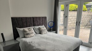 A modern bedroom with a large bed, a bedside table, a nightstand, and a view through a glass door to an outdoor area. - Private 2 Bedroom Apartment -edinburgh - Sleeps 4 (Edinburgh)