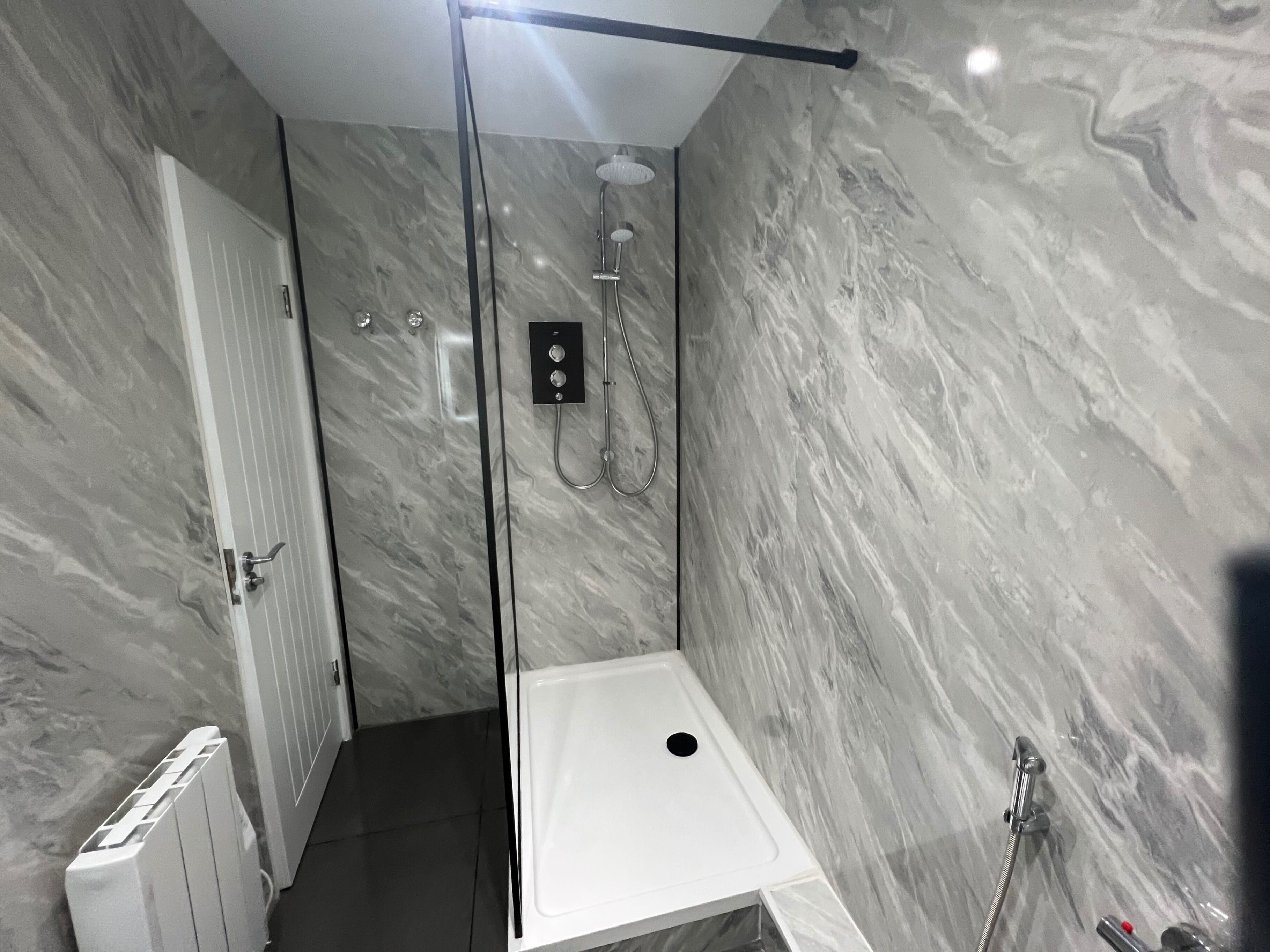 Une salle de bain moderne avec une douche en verre, des murs en marbre et un lavabo blanc.