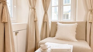 Una habitación con un sofá, una mesa con un libro y una taza, y cortinas atadas.