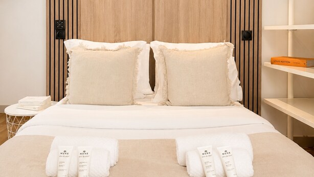 Habitación de hotel moderna con pared de panel de madera, dos lámparas de noche, cama con ropa blanca, mesita de noche con teléfono y estante con un libro.