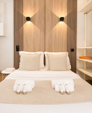 A modern hotel room with a wooden panel wall, two bedside lamps, a bed with white linens, a bedside table with a phone, and a shelf with a book. - 2063 Lille (Paris)