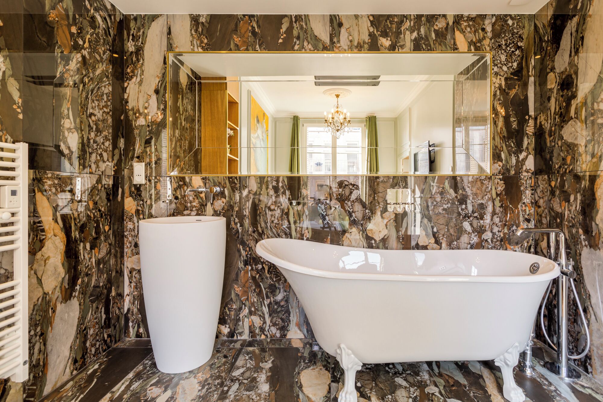 A bathroom with a freestanding bathtub, a large mirror, and a marble wall.