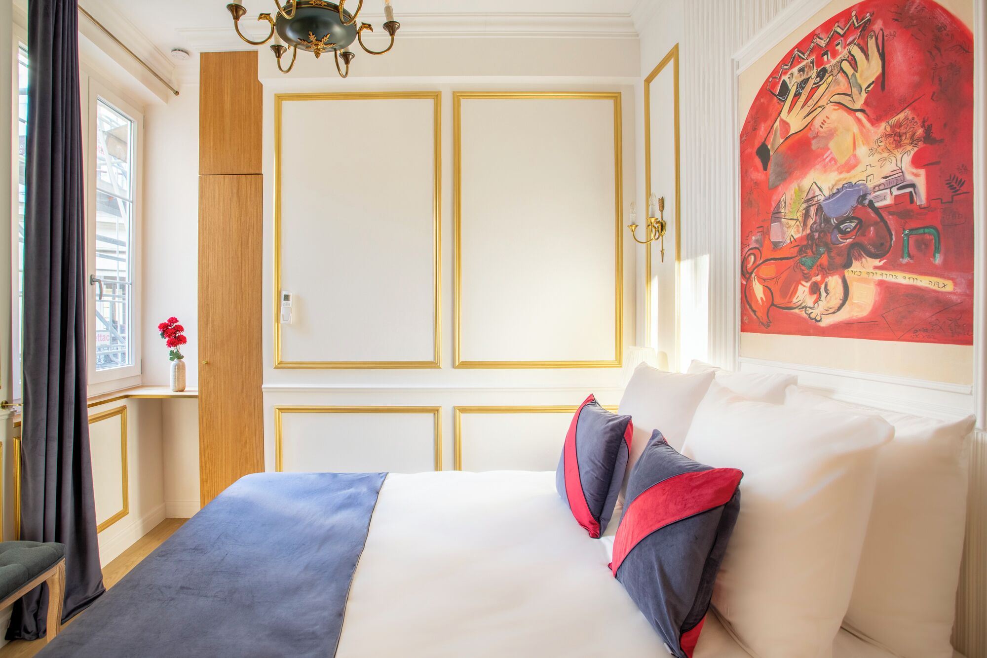Hotellihuone, jossa on suuri sänky, ikkuna, jossa on verhot, puinen vaatekaappi ja taulu seinällä.